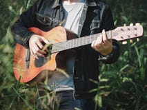 Músico considerável que joga a guitarra acústica no fundo do borrão do campo de grama Dia da música do mundo música e conceito do fotografia de stock Músico considerável que joga a guitarra acústica no fundo do borrão do campo de grama Dia da música do mundo música e conceito do fotografia de stock