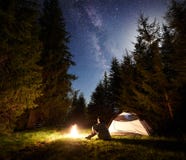 Męska wycieczkowicza enjoyng noc obozuje blisko turystycznego namiotu przy ogniskiem pod błękitnym gwiaździstym niebem i Milky sp fotografia royalty free Męska wycieczkowicza enjoyng noc obozuje blisko turystycznego namiotu przy ogniskiem pod błękitnym gwiaździstym niebem i Milky sp fotografia royalty free