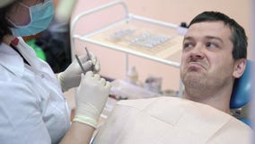 Męski pacjent kłama na stomatologicznym krześle w klinice, opowiada lekarka, ono uśmiecha się i przygotowywa dla procedur, zbiory Męski pacjent kłama na stomatologicznym krześle w klinice, opowiada lekarka, ono uśmiecha się i przygotowywa dla procedur, zbiory