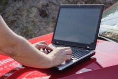 Mężczyzna używa laptop na kapiszonie samochód zdjęcie stock Mężczyzna używa laptop na kapiszonie samochód zdjęcie stock
