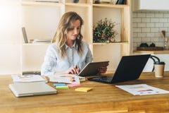Młoda bizneswoman kobieta siedzi przy kuchennym stołem i używa pastylka komputer, działanie, studiowanie fotografia royalty free Młoda bizneswoman kobieta siedzi przy kuchennym stołem i używa pastylka komputer, działanie, studiowanie fotografia royalty free