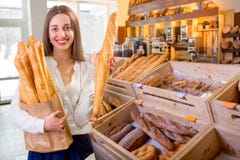 Młoda i uśmiechnięta kobieta z baguettes w piekarnia sklepie obraz stock Młoda i uśmiechnięta kobieta z baguettes w piekarnia sklepie obraz stock