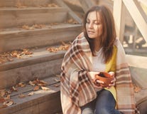 Młoda kobieta odpoczywa herbacianego obsiadanie w jesień ogródzie na krokach i pije, zawijających w woolen szkockiej kraty koc obrazy stock Młoda kobieta odpoczywa herbacianego obsiadanie w jesień ogródzie na krokach i pije, zawijających w woolen szkockiej kraty koc obrazy stock