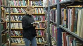 Młoda kobieta wybiera książkę w bibliotece Jest w korytarzu między książkami zbiory Młoda kobieta wybiera książkę w bibliotece Jest w korytarzu między książkami zbiory