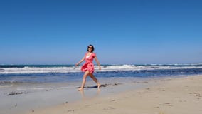 Młoda radosna kobieta chodzi wzdłuż plaży i rzuca jej kapeluszowych oddalonych jest ubranym czerwień okulary przeciwsłonecznych i zbiory Młoda radosna kobieta chodzi wzdłuż plaży i rzuca jej kapeluszowych oddalonych jest ubranym czerwień okulary przeciwsłonecznych i zbiory