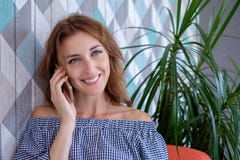 Młoda szczęśliwa kobieta opowiada na telefonie komórkowym z przyjacielem podczas gdy siedzący samotnie w nowożytnym sklep z kawą zdjęcia royalty free Młoda szczęśliwa kobieta opowiada na telefonie komórkowym z przyjacielem podczas gdy siedzący samotnie w nowożytnym sklep z kawą zdjęcia royalty free