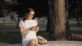 Młoda uśmiechnięta kobieta używa smartphone obsiadanie na ławce w parku przy zmierzchem Piękna europejska dziewczyna texting na t zbiory wideo Młoda uśmiechnięta kobieta używa smartphone obsiadanie na ławce w parku przy zmierzchem Piękna europejska dziewczyna texting na t zbiory wideo