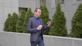 M?ody biznesmen chodzi z bezprzewodowymi he?mofonami w jego ucho i opowiada na wideo rozmowie na smartphone zdjęcie wideo M?ody biznesmen chodzi z bezprzewodowymi he?mofonami w jego ucho i opowiada na wideo rozmowie na smartphone zdjęcie wideo