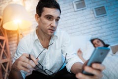 Młody biznesmen w białej koszula trzyma telefon i czytelniczych szkła w jego rękach Kobieta śpi w łóżku zdjęcie stock Młody biznesmen w białej koszula trzyma telefon i czytelniczych szkła w jego rękach Kobieta śpi w łóżku zdjęcie stock