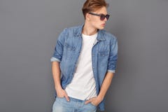 Młody człowiek w cajgach kurtka i okulary przeciwsłoneczni studio odizolowywający na popielaty patrzeć na boku chłodno obraz stock Młody człowiek w cajgach kurtka i okulary przeciwsłoneczni studio odizolowywający na popielaty patrzeć na boku chłodno obraz stock