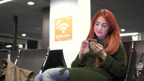 Młody szczęśliwy żeński używa telefon w lotniskowy śmiertelnie zbiory Młody szczęśliwy żeński używa telefon w lotniskowy śmiertelnie zbiory