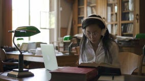 Młody żeńskiego ucznia prawnik jest czytelniczym książką, pisać na maszynie na laptopu obsiadaniu w bibliotece zbiory Młody żeńskiego ucznia prawnik jest czytelniczym książką, pisać na maszynie na laptopu obsiadaniu w bibliotece zbiory