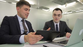 Młodzi człowiecy opowiada, używać laptop i pastylkę w wielkiej firmie zdjęcie wideo Młodzi człowiecy opowiada, używać laptop i pastylkę w wielkiej firmie zdjęcie wideo