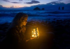 Nacht bij het strand, blondevrouw met lantaarn, golven van het overzees en wilde rotsvormingen op de achtergrond Stock Fotografie Nacht bij het strand, blondevrouw met lantaarn, golven van het overzees en wilde rotsvormingen op de achtergrond Stock Fotografie