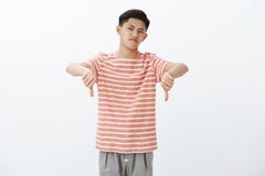 Nah giving negative feedback. Displeased and dissatisfied attractive young asian male in striped t-shirt showing thumbs stock photo Nah giving negative feedback. Displeased and dissatisfied attractive young asian male in striped t-shirt showing thumbs stock photo