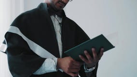 Nahaufnahme, indischer Hochschulabsolvent im Kleid, das ein Diplom hält und ihn betrachtet stock footage Nahaufnahme, indischer Hochschulabsolvent im Kleid, das ein Diplom hält und ihn betrachtet stock footage
