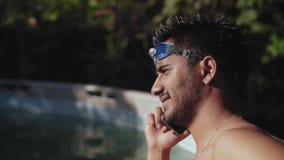 Nahaufnahme, indischer Kerl mit dem nackten Torso, der in einem Pool steht und am Telefon nachdem dem Tauchen spricht stock footage Nahaufnahme, indischer Kerl mit dem nackten Torso, der in einem Pool steht und am Telefon nachdem dem Tauchen spricht stock footage