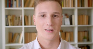 Nahaufnahmeporträt des jungen hübschen kaukasischen männlichen Studenten, der lächelt Kamera in der Collegebibliothek nett, betra stock footage Nahaufnahmeporträt des jungen hübschen kaukasischen männlichen Studenten, der lächelt Kamera in der Collegebibliothek nett, betra stock footage