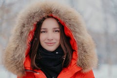 Naher hoher Schuss der attraktiven Frau trägt rote Jacke mit Kapuzenpulli, Schal, geht im Freien bei Winterfrostwetter, genießt E stockfotografie Naher hoher Schuss der attraktiven Frau trägt rote Jacke mit Kapuzenpulli, Schal, geht im Freien bei Winterfrostwetter, genießt E stockfotografie