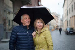 Nahes hohes Portr?t des ?lteren Mannes und seiner jungen blond-haarigen der Frau, die sich umfasst und unter ihrem Regenschirm st lizenzfreie stockfotos Nahes hohes Portr?t des ?lteren Mannes und seiner jungen blond-haarigen der Frau, die sich umfasst und unter ihrem Regenschirm st lizenzfreie stockfotos