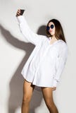 Naked girl in a man`s white shirt and sunglasses, holding phone, doing selfie. Naked girl in a man`s white shirt and sunglasses, holding phone, doing selfie Royalty Free Stock Image Naked girl in a man`s white shirt and sunglasses, holding phone, doing selfie. Naked girl in a man`s white shirt and sunglasses, holding phone, doing selfie Royalty Free Stock Image