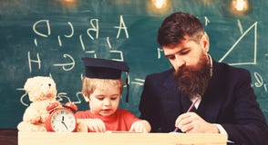 Nauczyciel w formalnej odzie?y i uczniu w mortarboard w sala lekcyjnej, chalkboard na tle Ojciec sprawdza prac? domow?, pomoce zdjęcia royalty free Nauczyciel w formalnej odzie?y i uczniu w mortarboard w sala lekcyjnej, chalkboard na tle Ojciec sprawdza prac? domow?, pomoce zdjęcia royalty free