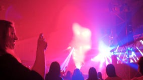 Nemend video van rotsoverleg, meisje die met omhoog handen dansen, menigte die door kleurrijke lichten wordt verlicht Nemend video van rotsoverleg, meisje die met omhoog handen dansen, menigte die door kleurrijke lichten wordt verlicht