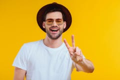netter junger Mann im weißen T-Shirt, im Hut und in der Sonnenbrille, die Siegeszeichen zeigt und an der Kamera lächelt stockbilder netter junger Mann im weißen T-Shirt, im Hut und in der Sonnenbrille, die Siegeszeichen zeigt und an der Kamera lächelt stockbilder