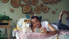 Nettes Mädchen nimmt selfie mit dem Haustier, das mit dem schönen Hund aufwirft, der auf dem Bett liegt, das Spaß und das Lachen stock video footage Nettes Mädchen nimmt selfie mit dem Haustier, das mit dem schönen Hund aufwirft, der auf dem Bett liegt, das Spaß und das Lachen stock video footage