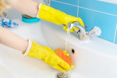 Nettoyage - évier et robinet de salle de bains de nettoyage avec le détergent dans y photo stock Nettoyage - évier et robinet de salle de bains de nettoyage avec le détergent dans y photo stock