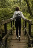 Girl crossing a bridge photographed from behind / Young girl with a backpack crossing a bridge in the forest stock images Girl crossing a bridge photographed from behind / Young girl with a backpack crossing a bridge in the forest stock images