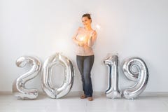 New 2019 Year is coming. Cheerful young woman standing near silver colored numbers and sparklers in white room stock images New 2019 Year is coming. Cheerful young woman standing near silver colored numbers and sparklers in white room stock images