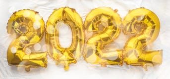 2022 new year numbers in golden foil balloons on white sheet background with festive lights bokeh