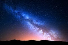 Night landscape with colorful Milky Way and yellow light at mountains. Starry sky with hills at summer. Beautiful Universe. Space