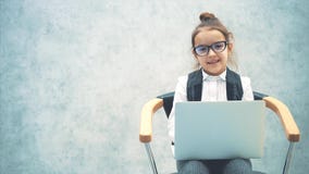 Niña de negocios sonriendo en el fondo gris. Durante este tiempo, el portátil se conserva. Sentado en la silla y almacen de video Niña de negocios sonriendo en el fondo gris. Durante este tiempo, el portátil se conserva. Sentado en la silla y almacen de video