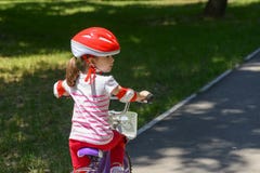Niña expresiva con el casco de seguridad rojo colorido que monta una bicicleta Imagenes de archivo Niña expresiva con el casco de seguridad rojo colorido que monta una bicicleta Imagenes de archivo