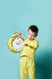 Niño pequeño lindo con el despertador, aislado en azul Niño divertido que señala en el despertador en la mañana fotos de archivo libres de regalías Niño pequeño lindo con el despertador, aislado en azul Niño divertido que señala en el despertador en la mañana fotos de archivo libres de regalías