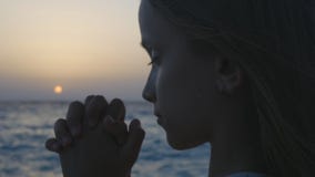 Niño que ruega en la playa en la puesta del sol, niño pensativo del rezo, muchacha pensativa en la playa foto de archivo Niño que ruega en la playa en la puesta del sol, niño pensativo del rezo, muchacha pensativa en la playa foto de archivo