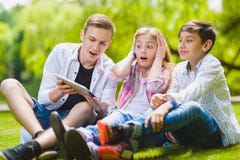 Niños sonrientes que tienen la diversión y mirada a hacer tabletas en la hierba Niños que juegan al aire libre en verano los adol fotografía de archivo Niños sonrientes que tienen la diversión y mirada a hacer tabletas en la hierba Niños que juegan al aire libre en verano los adol fotografía de archivo
