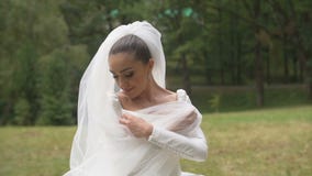 A noiva moreno atrativa bonita com sorriso bonito está envolvendo-se no véu no parque vídeos de arquivo A noiva moreno atrativa bonita com sorriso bonito está envolvendo-se no véu no parque vídeos de arquivo