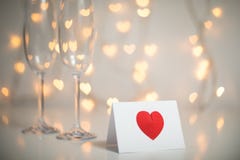 Nota romântica da mensagem com coração 3d vermelho nele, e champanhe com vidros e cordas claras feericamente com bokeh do coração fotos de stock Nota romântica da mensagem com coração 3d vermelho nele, e champanhe com vidros e cordas claras feericamente com bokeh do coração fotos de stock