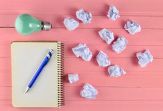 Notepad with a pen, incandescent bulb and crumpled white paper balls on a pink wooden table. Ideological concept, top view. stock photo Notepad with a pen, incandescent bulb and crumpled white paper balls on a pink wooden table. Ideological concept, top view. stock photo