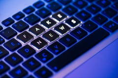 Noticias falsas escritas en un teclado retroiluminado en una luz ambiant azul Fotos de archivo libres de regalías Noticias falsas escritas en un teclado retroiluminado en una luz ambiant azul Fotos de archivo libres de regalías