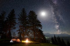 Notte maschio del enjoyng della viandante che si accampa vicino alla tenda turistica al fuoco di accampamento in corso il cielo e fotografia stock Notte maschio del enjoyng della viandante che si accampa vicino alla tenda turistica al fuoco di accampamento in corso il cielo e fotografia stock
