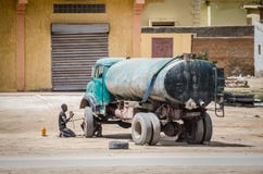 Nouakchott Mauretanien - Oktober 08 2013: Gataplats av det ändrande däcket för oidentifierad man på den gamla vattenlastbilen royaltyfri fotografi Nouakchott Mauretanien - Oktober 08 2013: Gataplats av det ändrande däcket för oidentifierad man på den gamla vattenlastbilen royaltyfri fotografi