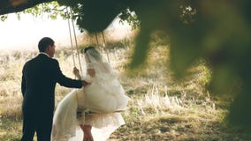 Novio feliz que balancea en un oscilación a la novia en el parque en verano : oscilación del muchacho y de la muchacha en a metrajes Novio feliz que balancea en un oscilación a la novia en el parque en verano : oscilación del muchacho y de la muchacha en a metrajes