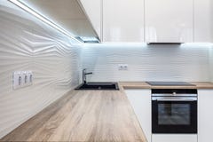 Nuova cucina moderna luminosa con costruito nel rubinetto di acqua del cromo e del forno ed in un piano d'appoggio di legno Fotografia Stock Nuova cucina moderna luminosa con costruito nel rubinetto di acqua del cromo e del forno ed in un piano d'appoggio di legno Fotografia Stock