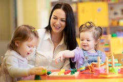 Nursery teacher looking after children in daycare. Little kids toddlers play together with developmental toys. stock photo Nursery teacher looking after children in daycare. Little kids toddlers play together with developmental toys. stock photo