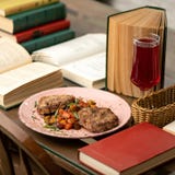 Nutritious Lunch at workplace. Plate with Fried minced meat cutlet and vegetables on table with drink glass and books on