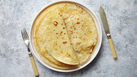 Nya hemlagade kräppar, tunna pannkakor som förläggas på den vita ceramiceplattan Nya hemlagade kräppar, tunna pannkakor som förläggas på den vita ceramiceplattan